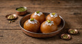 Four golden-brown gulab halwa desserts in a hammered copper plate, garnished with silver foil and pistachios, on a rustic wooden table with small copper bowls cardamom seeds.